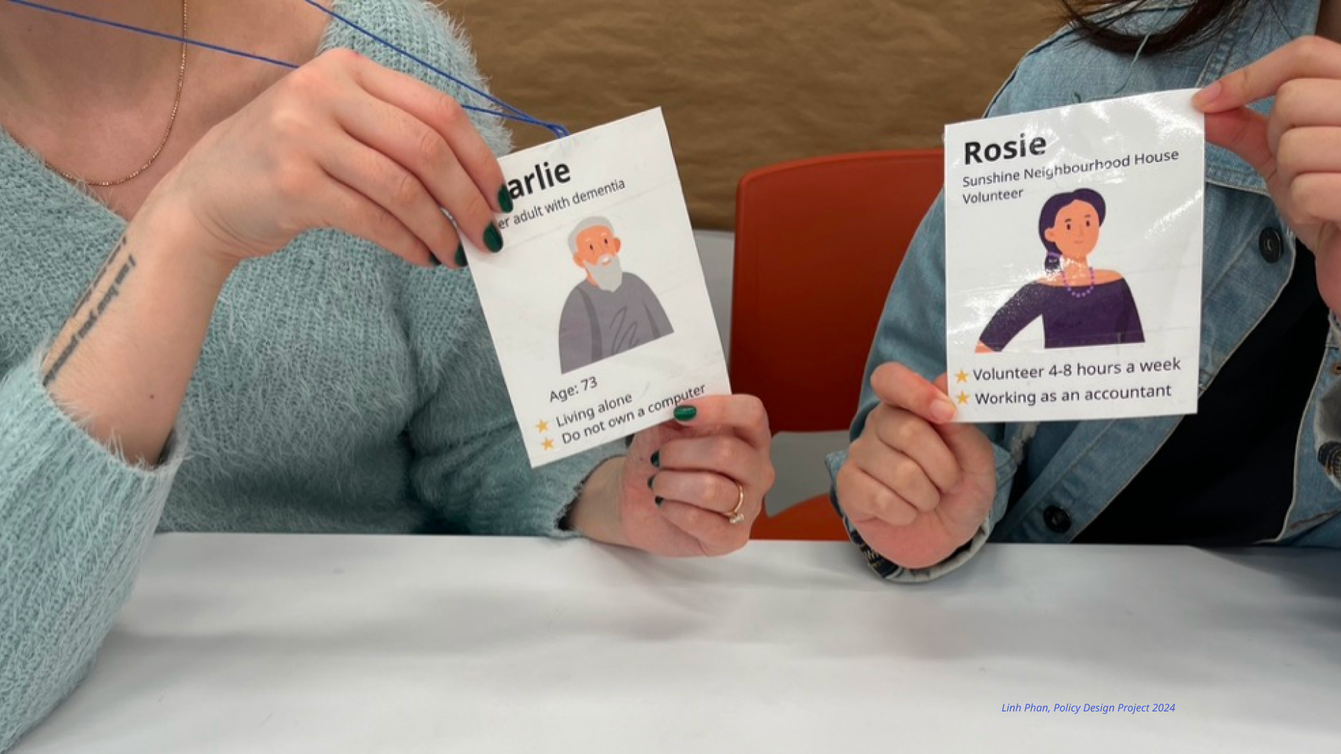 Example of Roleplay activity in the workshops. Two person wearing character tag facing each other. The first person wear a tag for a character name Charlie, who is an older adult with dementia, live alone and don't have access to the computer. The second person is wearing a tag for a character name Rosie, who is a volunteer for Sunshine Neighbourhood House. This activity aims to simulate future scenarios in order to find area of improvements for the service