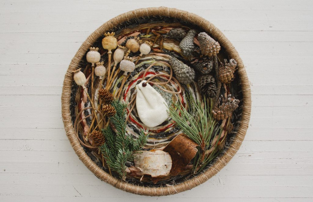 A handwoven tray with lodgepole pine cones, a white deerskin medicine pouch, poppy pods, spruce cones, pine cones and birch bark.