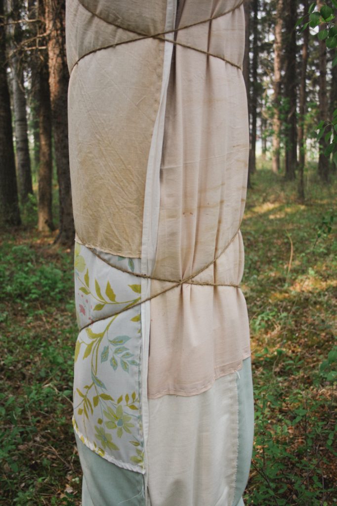 A close-up photograph of a handmade patchwork blanket on a black spruce tree in a forest.