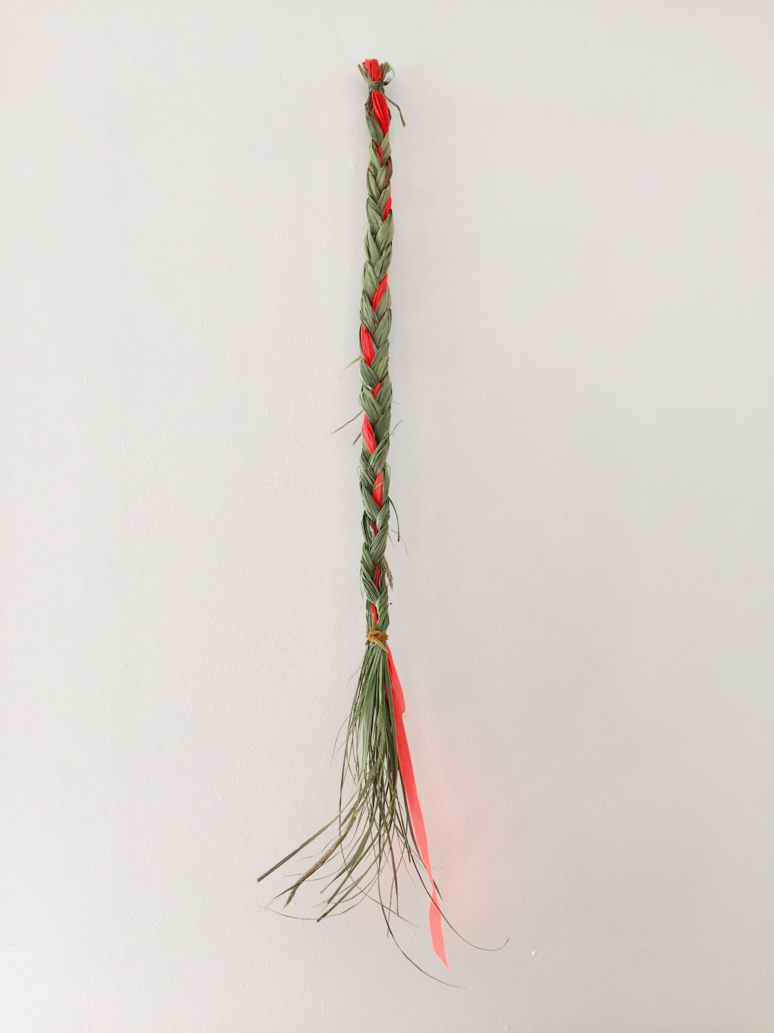 Braided Sweetgrass with a piece of orange flagging tape woven into it.
