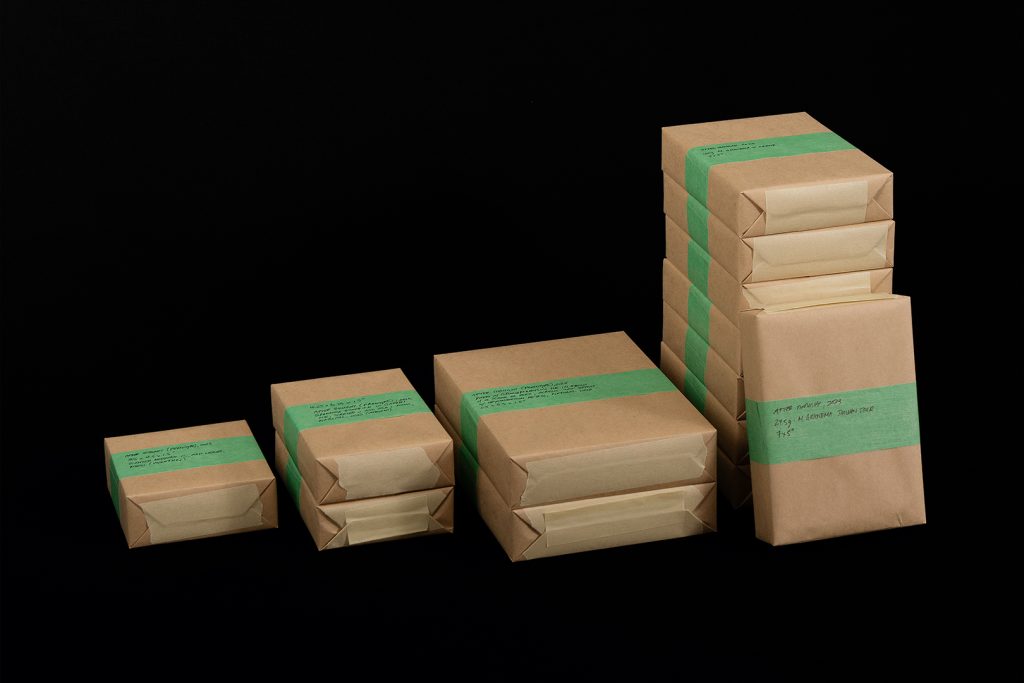 "After Care" (2023) is a photographic print depicting neatly wrapped, taped, and labeled brown paper packages.