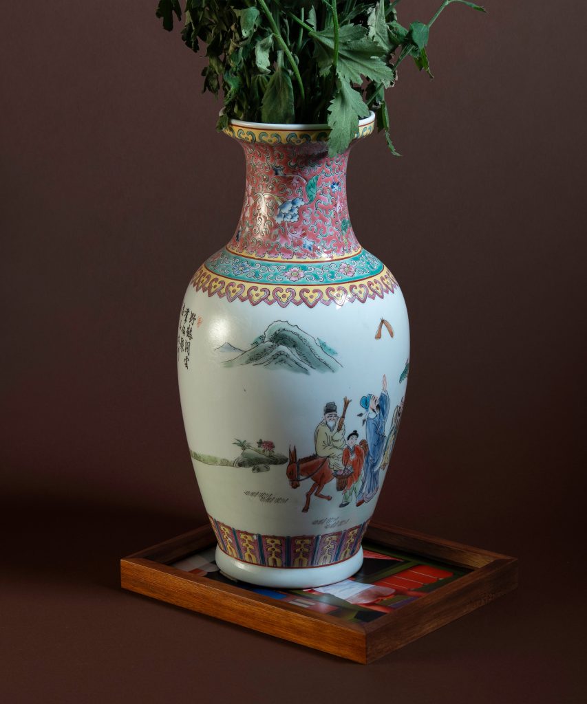 Image of "Florid Scale" (2023), a photographic work depicting a traditional Chinese decorative vase holding wilted flowers. The vase sits atop an unprotected image in a glass-less wooden frame.