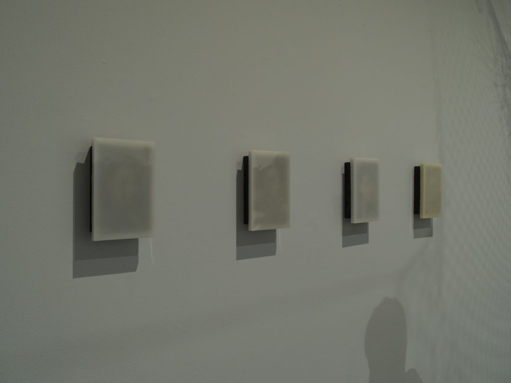 Installation view of "Precipitant" (2024), an artwork consisting of four portraits mounted onto burnt wood, each encased in a thick layer of wax.