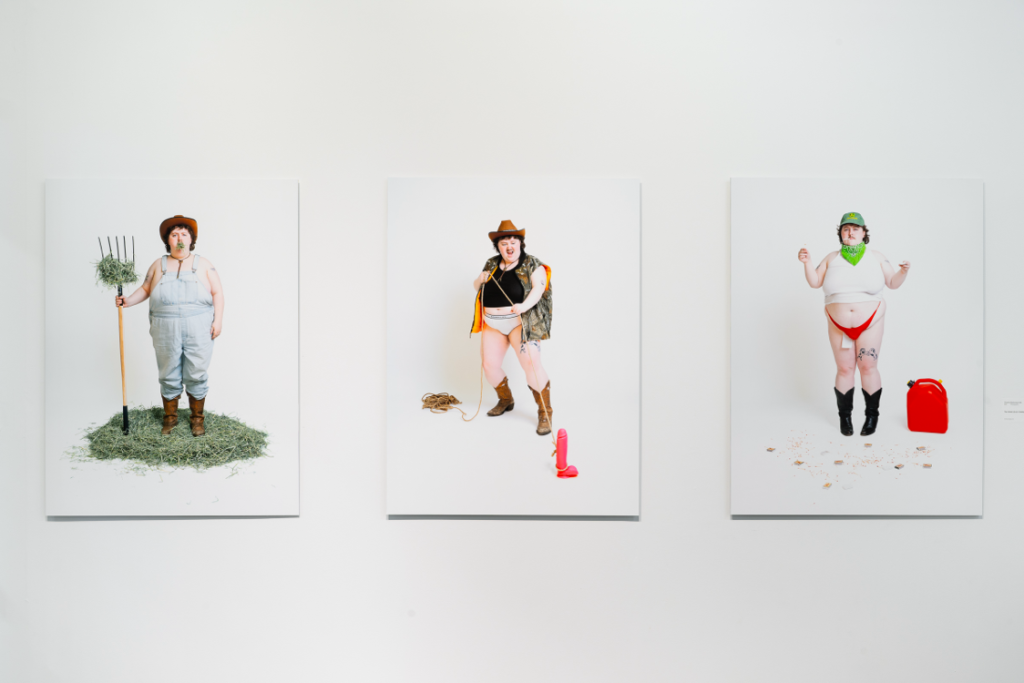 Installation view of 3 similar photographic works showing the same person posting in rural scenes on white backgrounds with some incongruent elements.