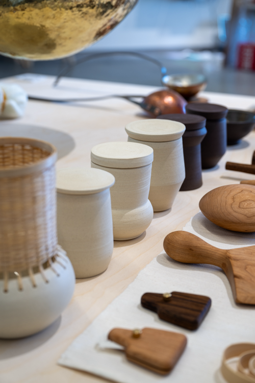Closeup of various ceramic and wood works including covered cups on a table. 